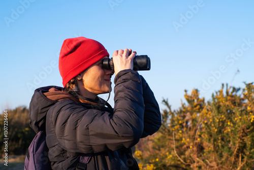 Photography A young girl in a red hat watches birds and wild animals with binoculars in the bushes on a sunny day in spring