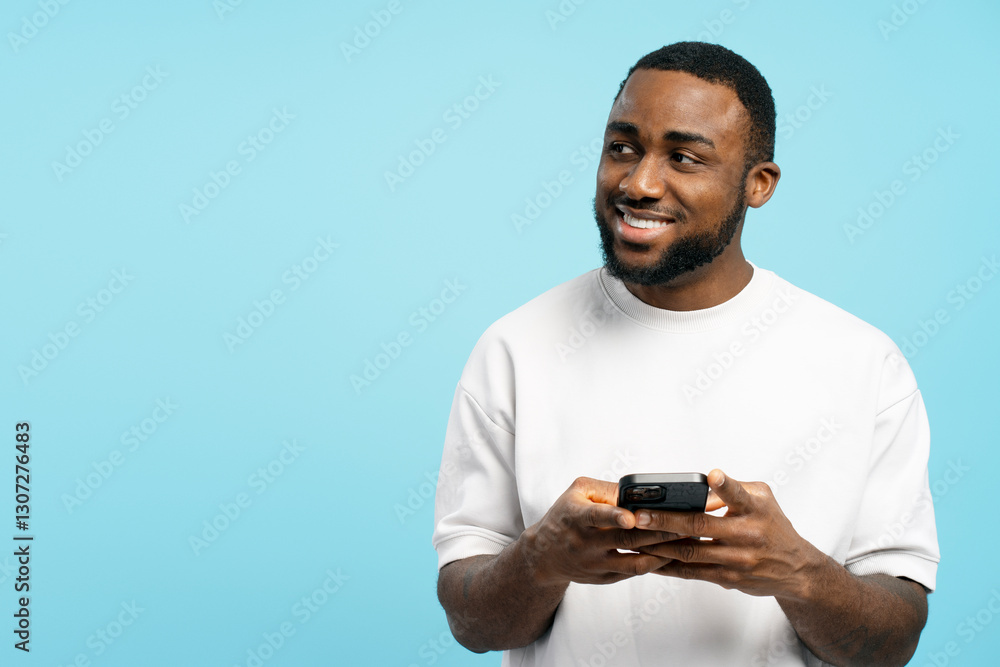 Young man using smartphone and smiling while looking away on blue background