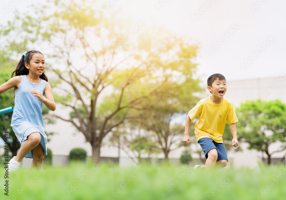Two young children running in a relay race in a park on a sunny summer day Two young children running in a relay race in a park on a sunny summer day