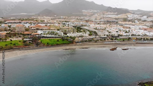 Aerial view of Costa Adeje city, Tenerife, Canary islands. Cinematic 4K footage with sandy coast, calm waters of Atlantic ocean, city modern villas, quay, mountains. Video during sandy storm calima