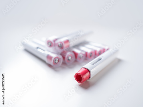 bright composition with many pen injectors with a red tip for biological treatments such as Adalimumab, Etanercept or epinephrine. The background is aseptic, clean, white and well lit.