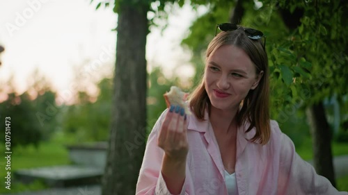 Wallpaper Mural Close-up of woman smiling while holding bread in hand and enjoying outdoor meal, seated in lush green park, with tattooed hand holding bread partially visible in background Torontodigital.ca
