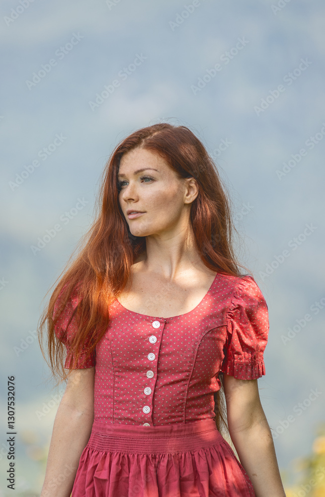 Schönes, rothariges Mädchen im Dirndl auf einer Wiese vor Bergkulisse Schönes, rothariges Mädchen im Dirndl auf einer Wiese vor Bergkulisse