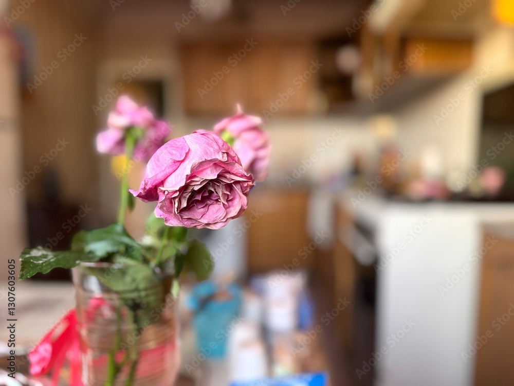 Obraz premium Faded pink roses stand in a vase in the kitchen under the sun's rays