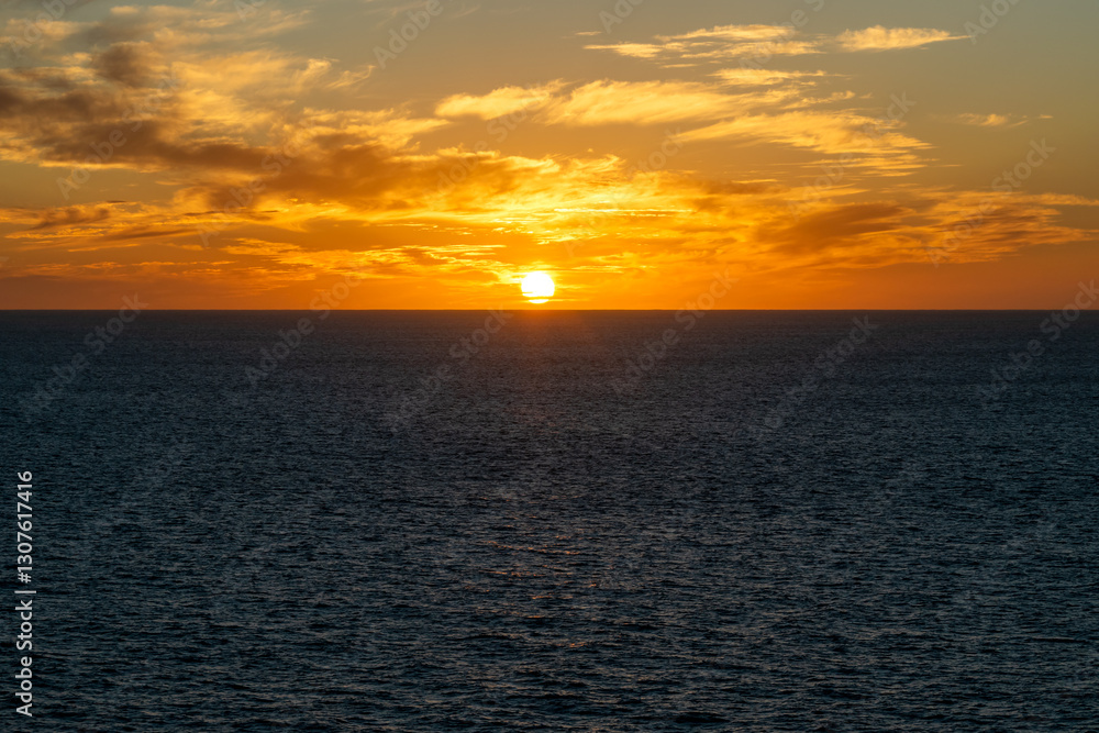 Bright sun at sunset on the horizon over the Pacific Ocean. The sky has an orange pattern and some reflections are visible on the sea.