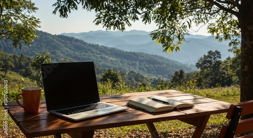 Working outdoors at a wooden table with laptop, notebook, and coffee surrounded by mountains