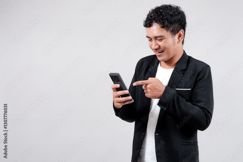 Asian man in a black blazer and white t-shirt using a smartphone with a happy expression. Isolated on a gray background. Concept of technology, communication, and business. Asian man in a black blazer and white t-shirt using a smartphone with a happy expression. Isolated on a gray background. Concept of technology, communication, and business.