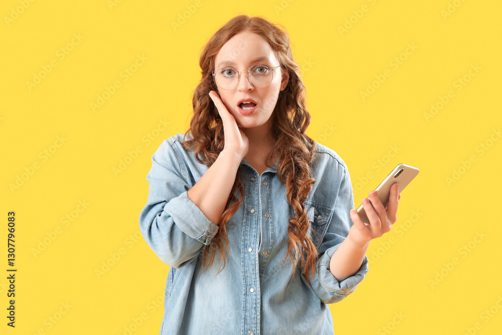 Shocked young redhead woman with mobile phone on yellow background Shocked young redhead woman with mobile phone on yellow background