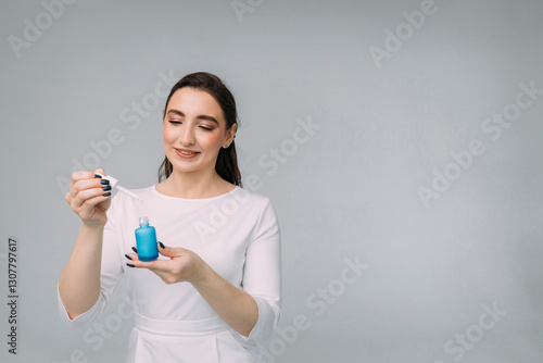 girl cosmetologist with long hair in a white dress holds a blue jar with facial serum in her hands