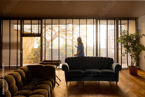 Obraz na plátne A woman in a blue outfit enjoys a peaceful morning by the large window with wooden blinds