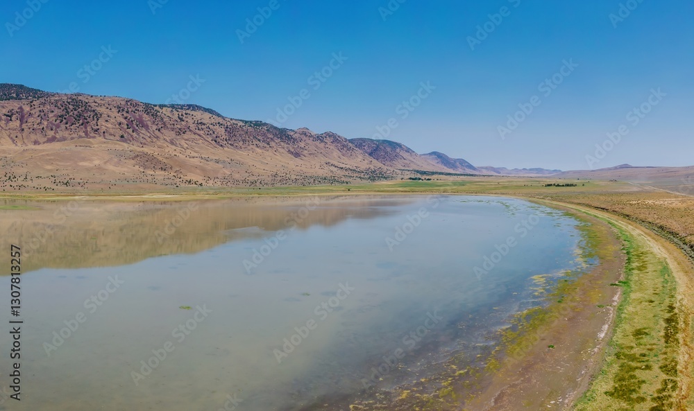 Aerial view of a Juniper Lake in the USA, reflecting the surrounding mountains and clear blue sky. The lake's surface shows patterns of aquatic vegetation. Princeton, Oregon, USA Aerial view of a Juniper Lake in the USA, reflecting the surrounding mountains and clear blue sky. The lake's surface shows patterns of aquatic vegetation. Princeton, Oregon, USA