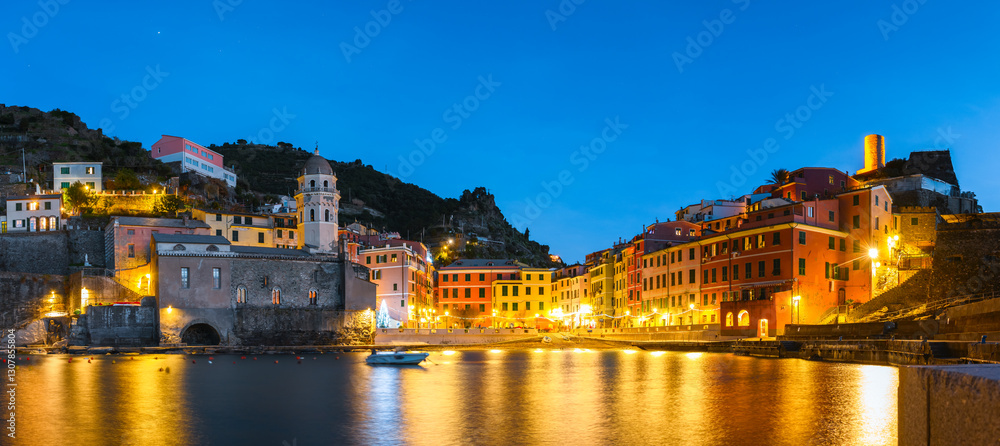 Fototapeta premium Panoramic view on fishing village Vernazza with glowing multicolored houses and blue evening sky. Cinque Terre National park, Liguria, Italy. Landscape photography
