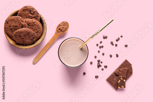 Glass of sweet chocolate milk and bowl with tasty cookies on pink background