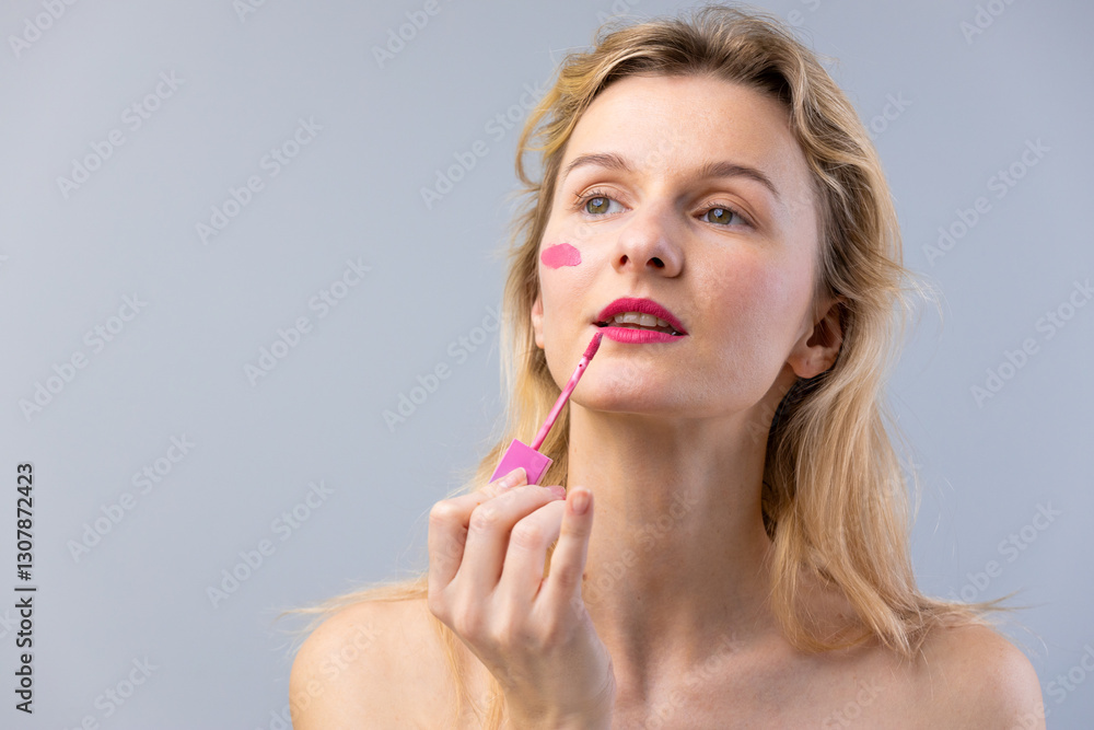 A Woman Applying Bright Pink Lipstick with a Playful Attitude and a Soft Touch in a Minimalist Studio Setting Reflecting Modern Beauty Trends and Self-Expression through Makeup. A Woman Applying Bright Pink Lipstick with a Playful Attitude and a Soft Touch in a Minimalist Studio Setting Reflecting Modern Beauty Trends and Self-Expression through Makeup.