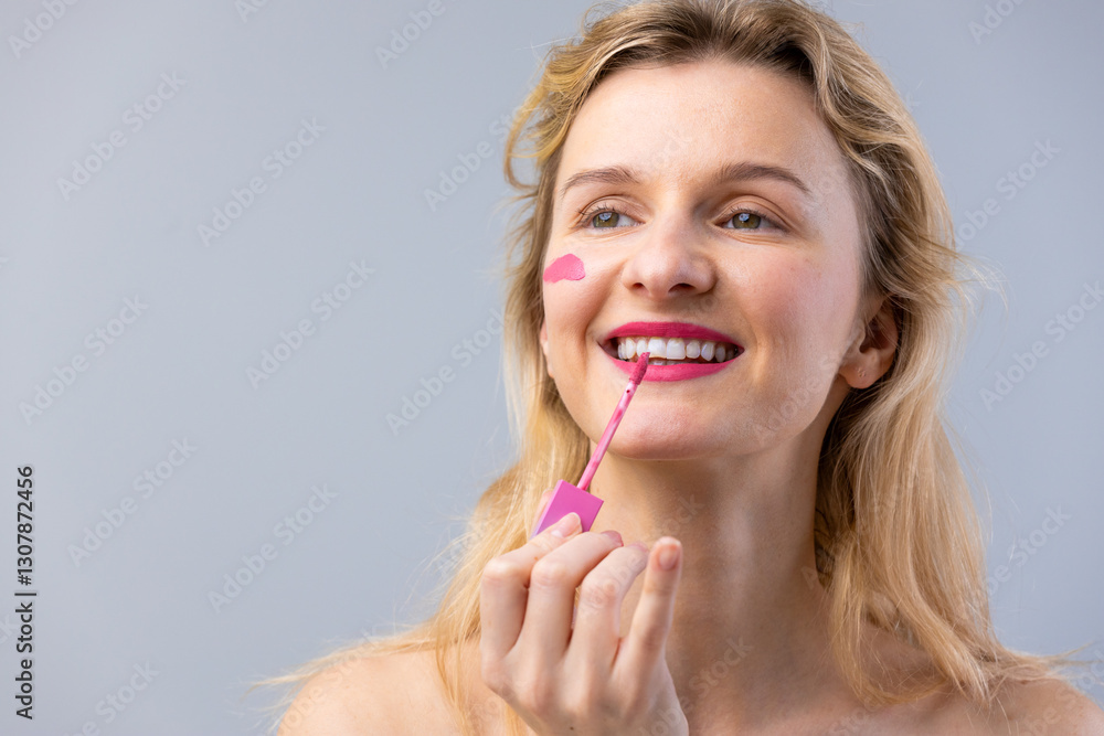 Young Woman Applying Bright Pink Lipstick with a Cheerful Smile, Showcasing Makeup Artistry and Self-Care in a Soft Blue Background for a Fashion or Beauty Editorial Young Woman Applying Bright Pink Lipstick with a Cheerful Smile, Showcasing Makeup Artistry and Self-Care in a Soft Blue Background for a Fashion or Beauty Editorial
