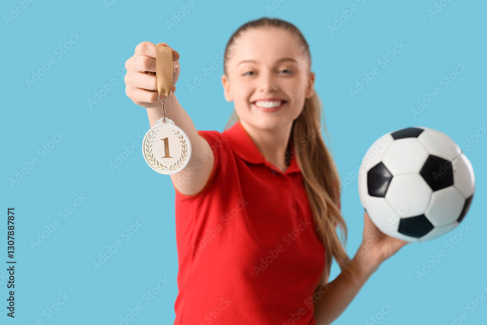 Sporty young woman with soccer ball and medal on blue background Sporty young woman with soccer ball and medal on blue background