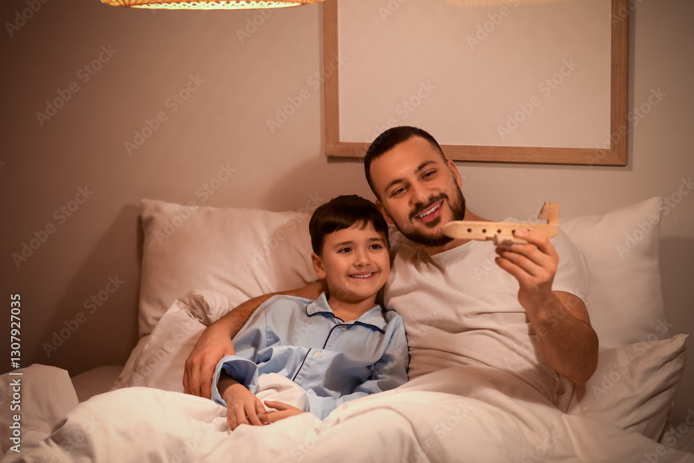 Fototapeta premium Father and his little son playing with wooden airplane before bedtime at home