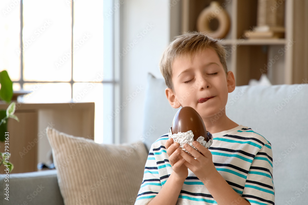 Little boy licking his lips and holding chocolate egg in living room Little boy licking his lips and holding chocolate egg in living room