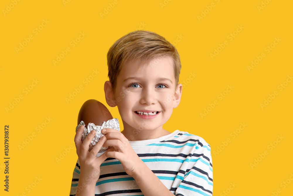 Smiling little boy with chocolate egg on yellow background Smiling little boy with chocolate egg on yellow background