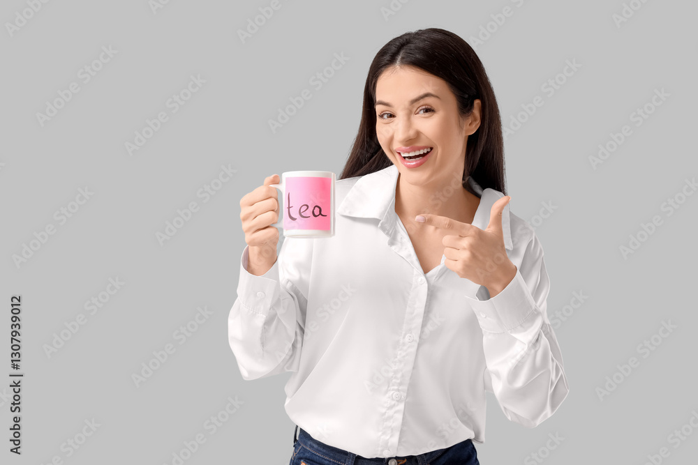 Beautiful young woman holding cup with word TEA on grey background Beautiful young woman holding cup with word TEA on grey background