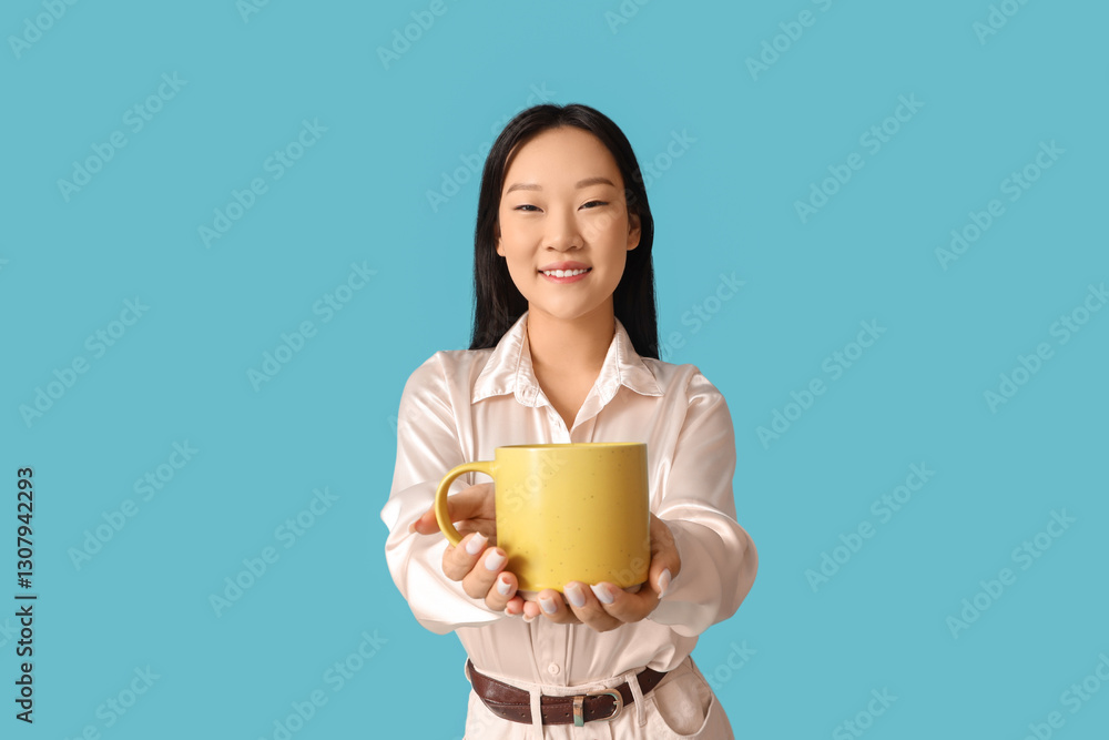 Young Asian woman drinking coffee from yellow mug on blue background Young Asian woman drinking coffee from yellow mug on blue background