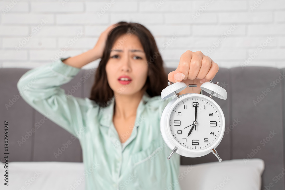 Stressed young Asian woman with alarm clock in bedroom, closeup Stressed young Asian woman with alarm clock in bedroom, closeup