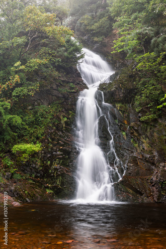 Majestic Waterfall Cascading Down Rocky Cliffs at Glencorse Burn, Pentland Hills Regional Park, Scotland, Surrounded by Lush Greenery and Misty Woodland in a Serene Natural Landscape