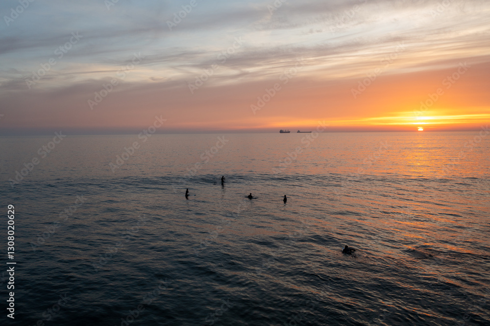 Obraz premium Aerial drone shot of silhouette anonymous people swimming in vast ocean against cloudy sky during sunset. Distant view of tourists amidst seascape enjoying vacation at sundown 