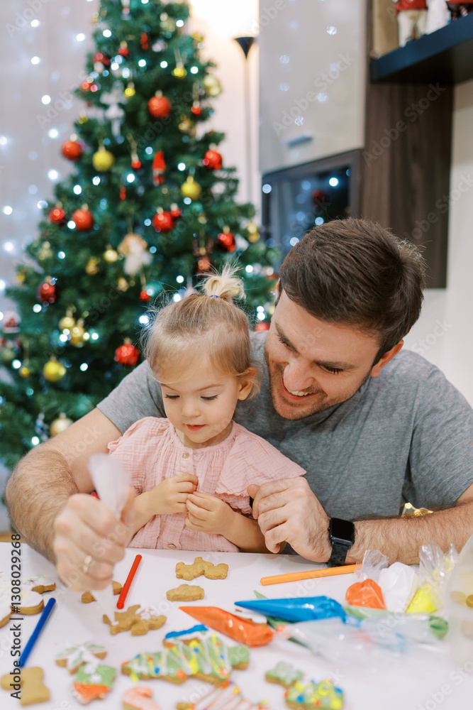 Little girl sitting on dad lap icing Christmas cookies Little girl sitting on dad lap icing Christmas cookies