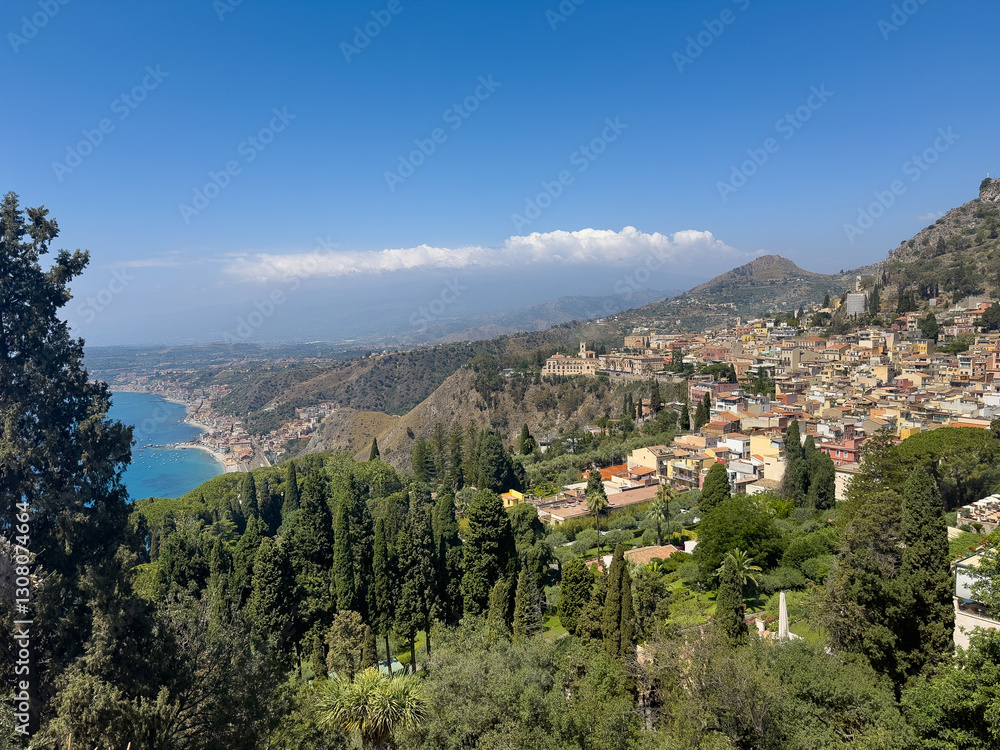 Obraz premium Taormina, Sicily, Italy - July 5, 2024: Looking west from Ancient Greek theatre or Teatro antico shows wide landscape with historic downtown, the sea on one side and mountains on other side under blue