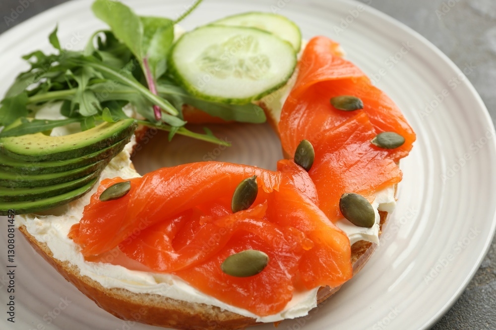 Delicious bagel with salmon, cream cheese, cucumber, avocado and pumpkin seeds on table, closeup Delicious bagel with salmon, cream cheese, cucumber, avocado and pumpkin seeds on table, closeup