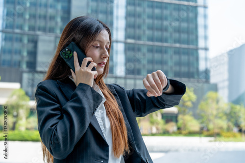 Wallpaper Mural businesswoman checks her watch while talking on phone outside modern office building, conveying sense of urgency and professionalism Torontodigital.ca