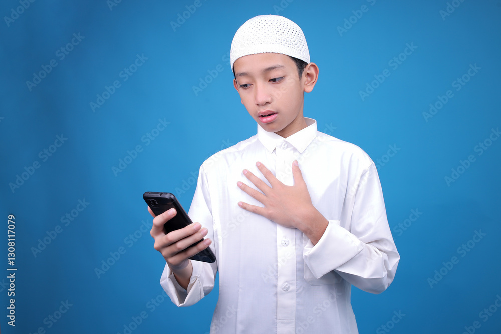 Shocked Young Boy Touching Chest While Looking At Smartphone Reading News Isolated On Blue Background Shocked Young Boy Touching Chest While Looking At Smartphone Reading News Isolated On Blue Background