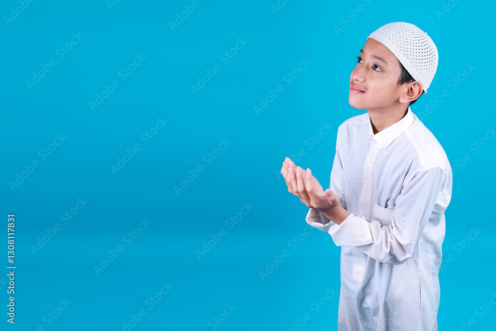 High Angle Of Young Teenage Boy Wear Muslim Clothes Raising Hands Praying Isolated On Blue Background