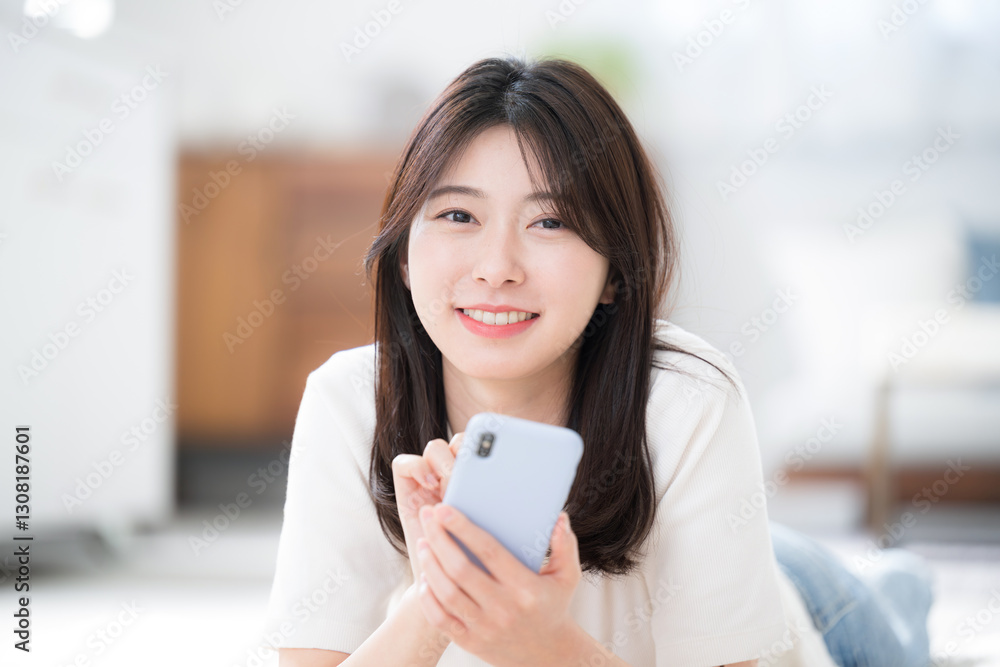 部屋でうつ伏せでスマホを見る若い女性のクローズアップ 春夏の半袖カメラ目線 部屋でうつ伏せでスマホを見る若い女性のクローズアップ 春夏の半袖カメラ目線
