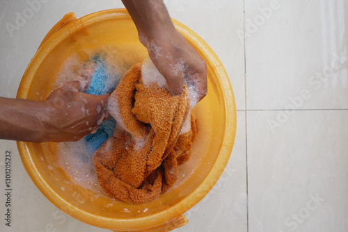Quadro su tela Hands washing cloth in orange tub filled with soap and water