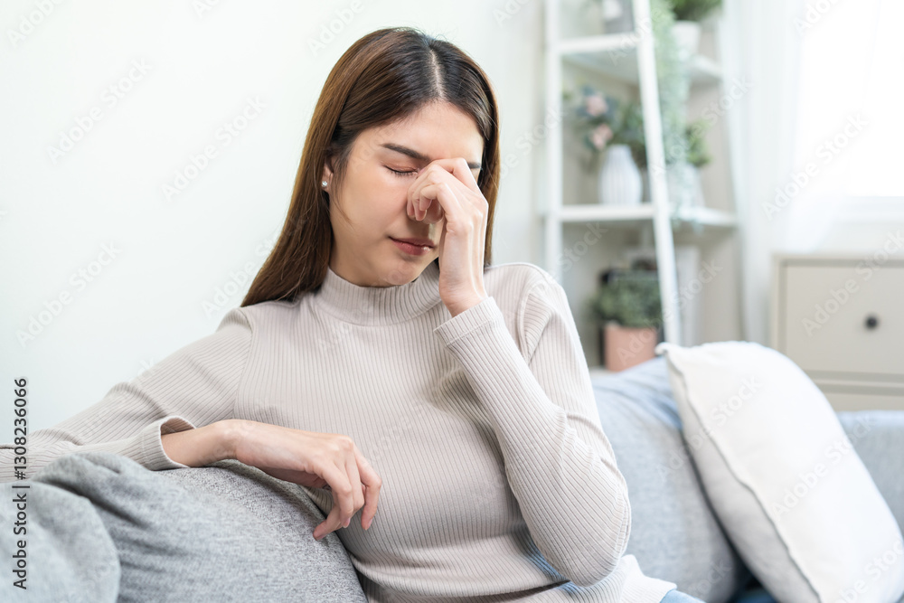 Depressed anxiety asian young woman, girl frustrated closed eyes, touching nose suffering stressed, sick, tired, crisis sitting on sofa from headache, migraine pain tension problem health care concept Depressed anxiety asian young woman, girl frustrated closed eyes, touching nose suffering stressed, sick, tired, crisis sitting on sofa from headache, migraine pain tension problem health care concept