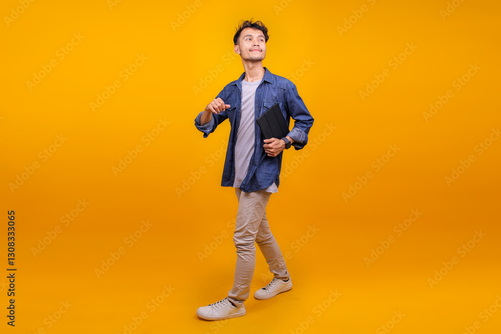 Full Length Of Happy Asian Man Holding Tablet And Walking While Looking Aside