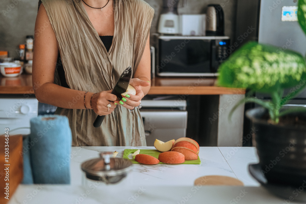 Close up of hands of young woman standing in kitchen at home cutting fresh red apple at table. She holds a knife and peels an apple preparing a healthy snack. Vegan product. Diet and healthy eating. Close up of hands of young woman standing in kitchen at home cutting fresh red apple at table. She holds a knife and peels an apple preparing a healthy snack. Vegan product. Diet and healthy eating.