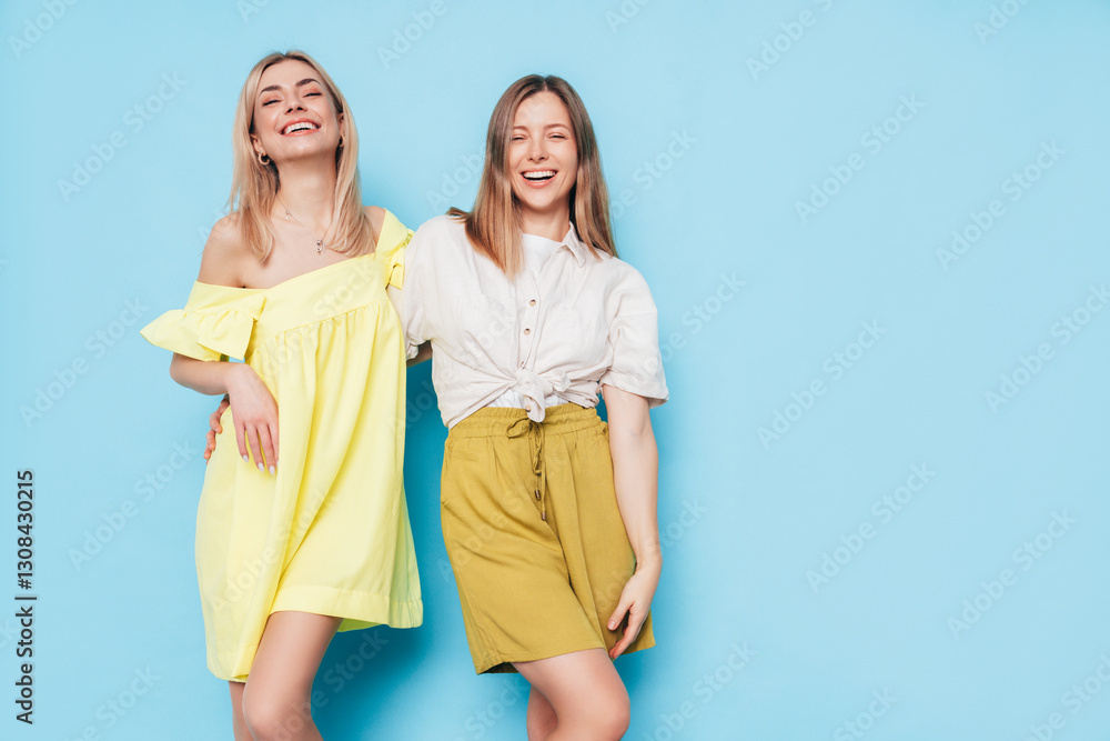 Two young beautiful smiling brunette and blond hipster female in trendy summer clothes. Lovely women posing on blue background in studio. Positive models having fun. Cheerful and happy. isolated Two young beautiful smiling brunette and blond hipster female in trendy summer clothes. Lovely women posing on blue background in studio. Positive models having fun. Cheerful and happy. isolated