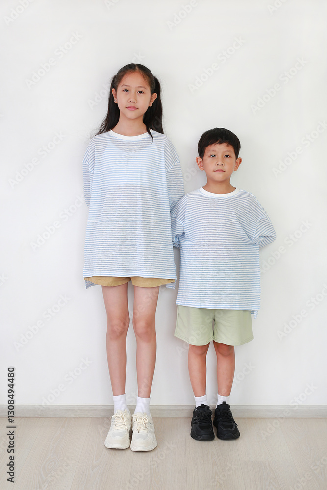 Portrait of Asian girl and boy standing and looking at camera against white wall in the room. Portrait of Asian girl and boy standing and looking at camera against white wall in the room.