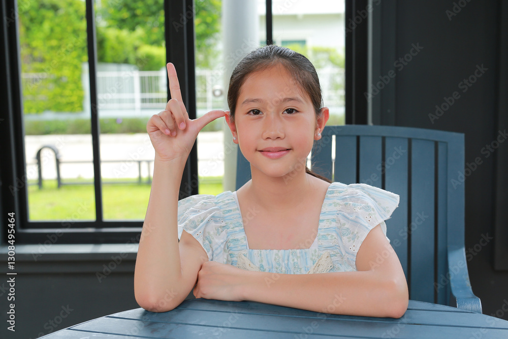 Portrait of young Asian girl show index finger up while sitting on chair in pavilion.