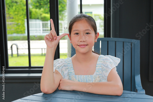 Obraz na płótnie Portrait of young Asian girl show index finger up while sitting on chair in pavilion. w salonie