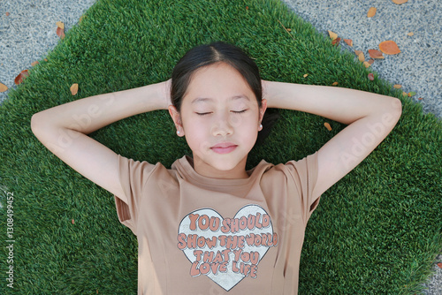 Obraz na płótnie Close-up top view of Asian girl child lying on green grass outdoors in summer park. Kid closed eyes resting in garden. w salonie