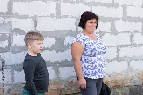 Photos This outdoor shot features a woman and a young boy standing side-by-side against a cinderblock wall