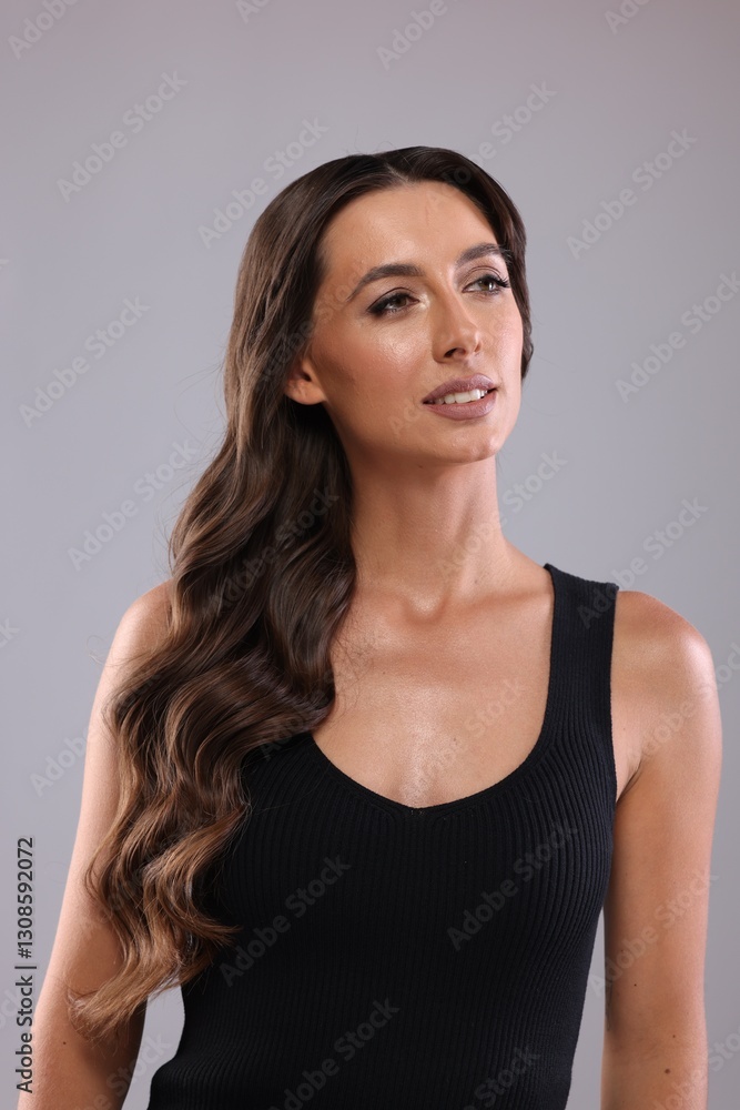 Hair styling. Beautiful woman with wavy long hair on grey background Hair styling. Beautiful woman with wavy long hair on grey background