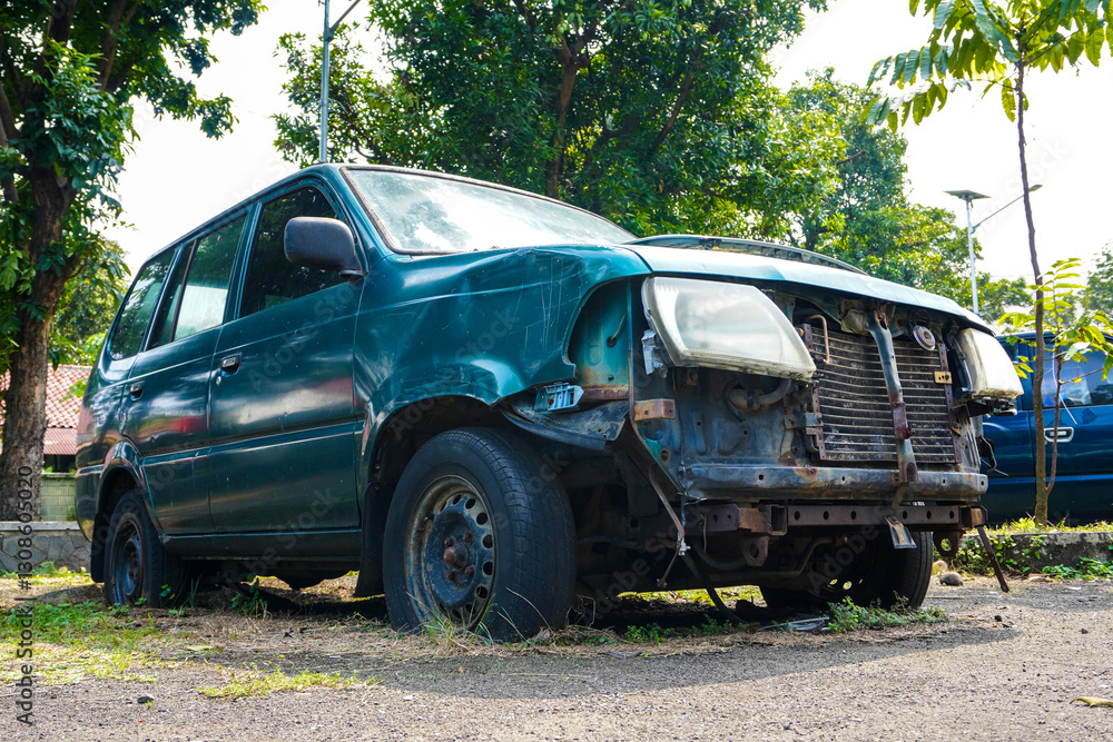 Abandoned green vehicle with missing parts and flat tires on overgrown lot in bright daylight Abandoned green vehicle with missing parts and flat tires on overgrown lot in bright daylight