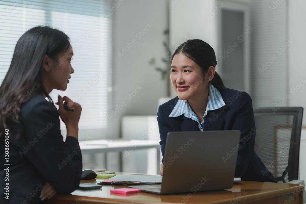 Two businesswomen discussing a project using laptop in office Two businesswomen discussing a project using laptop in office