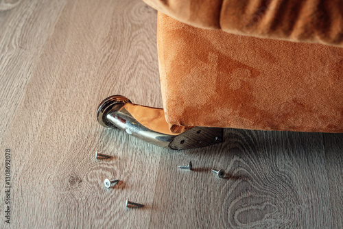 Photography A broken metal leg of a sofa with scattered screws on a wooden floor, symbolizing furniture damage and the need for urgent repair