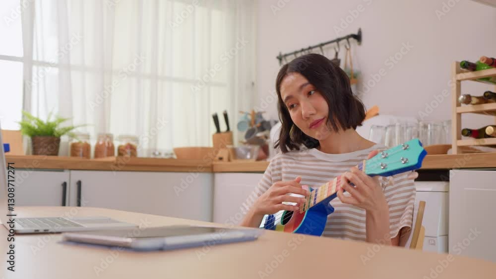 Asian woman learning to play ukulele through online tutorial on laptop. Asian woman learning to play ukulele through online tutorial on laptop.